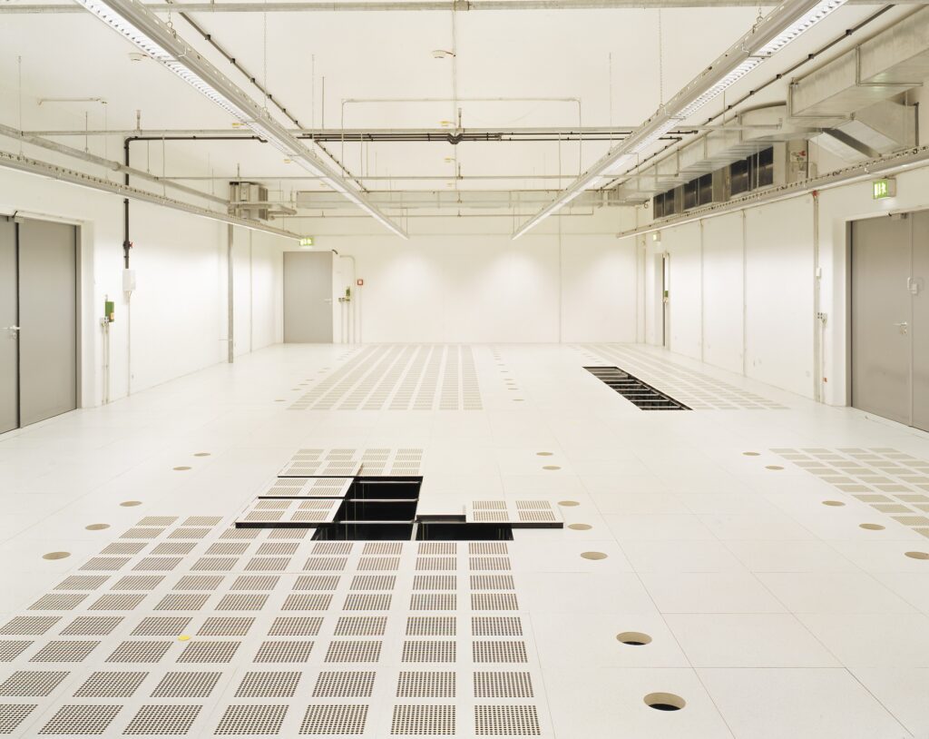 Stort teknisk rom med perforerte paneler i datagulv og åpne moduler for tilgang til installasjoner.
