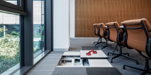 Installasjonsgulv i moderne kontorrom med åpnet gulvmodul som viser tekniske installasjoner under overflaten.