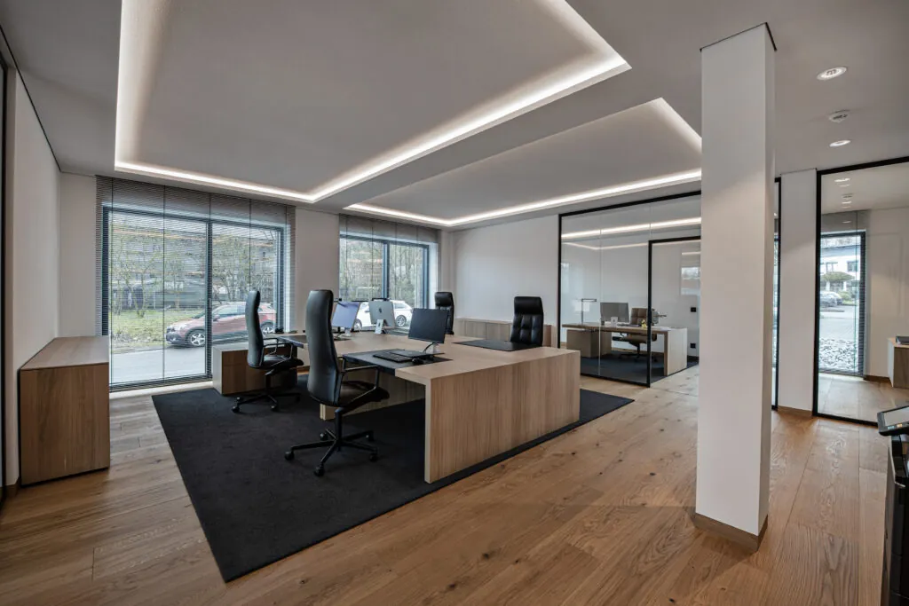 Open-plan office with large window surfaces, workstations and wooden flooring.