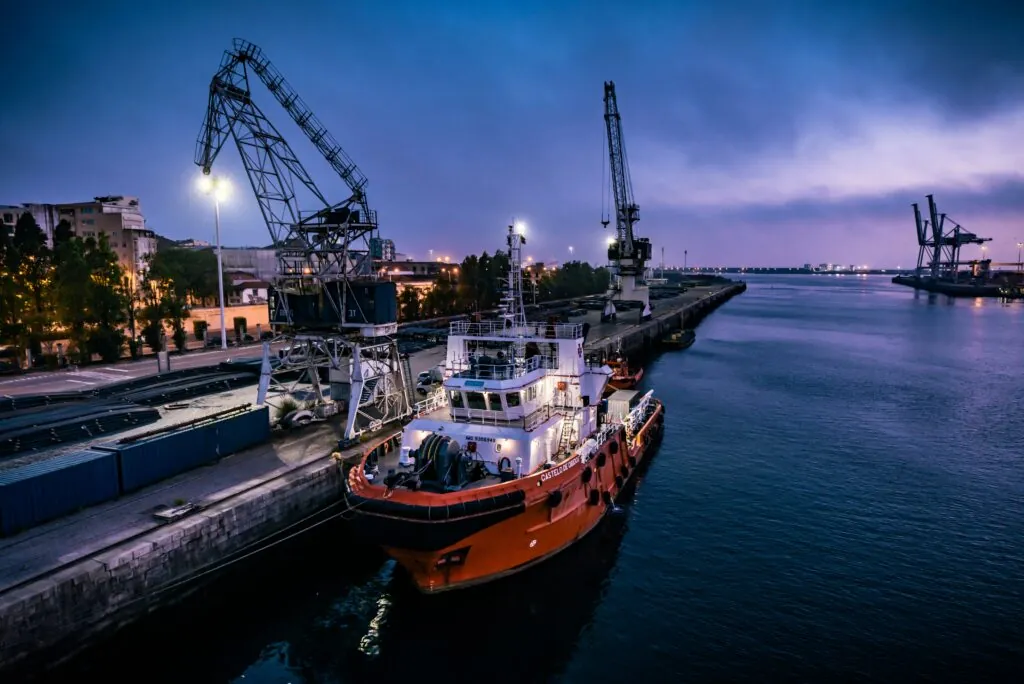 Maritime vessel docked at port with cranes and industrial surroundings, related to technical and maritime installations.