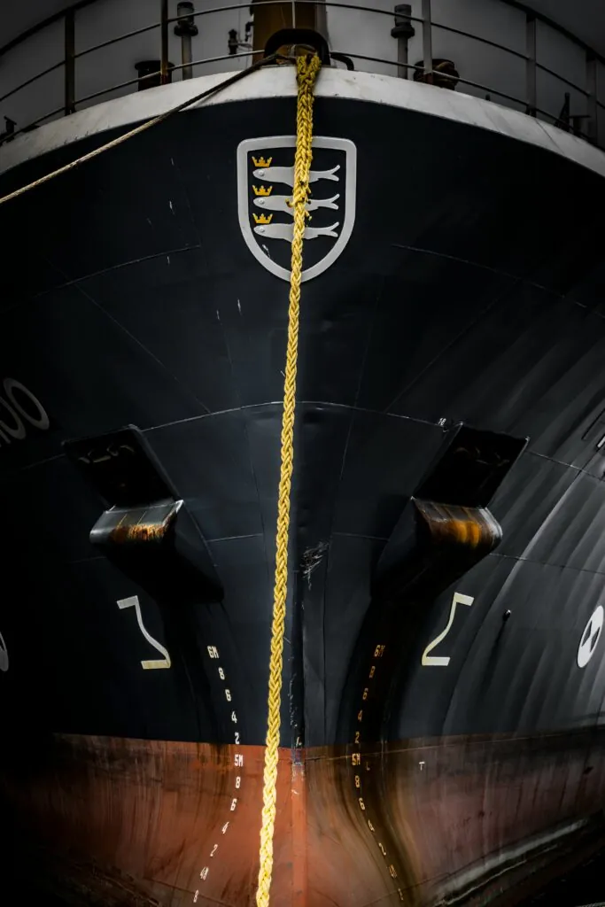 Bow of a maritime vessel at port with mooring lines and ship markings, related to maritime installations and technical environments.