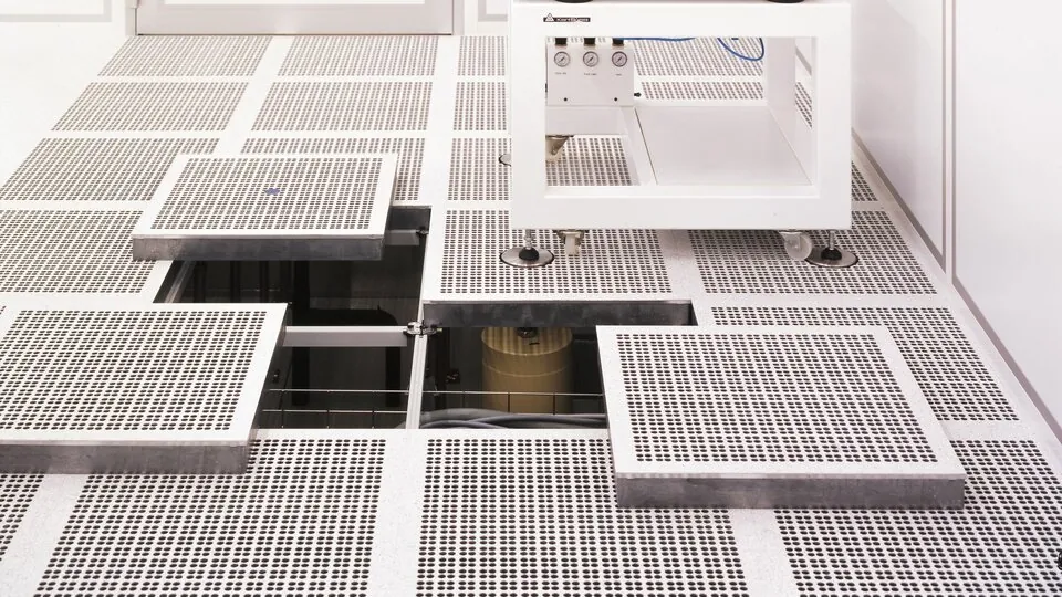 Hevet installasjonsgulv med perforerte ventilasjonsplater i renrom, med åpne gulvluker som viser teknisk infrastruktur under gulvnivå