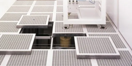 Hevet installasjonsgulv med perforerte ventilasjonsplater i renrom, med åpne gulvluker som viser teknisk infrastruktur under gulvnivå