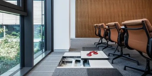 Installasjonsgulv i moderne kontorrom med åpnet gulvmodul som viser tekniske installasjoner under overflaten.